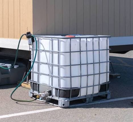 Large white water storage tank in a metal cage with a pump and green hose.